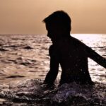 A boy standing in waist deep water in the river at early morning