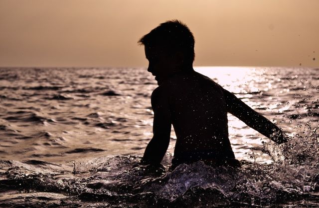 A boy standing in waist deep water in the river at early morning